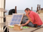 Gregg Stephens on the Firelands Winery dock with his homemade solar panel setup. The green round items are the individual cells of his battery packs, which he also made. Hams call constructing one's own equipment "home brewing."